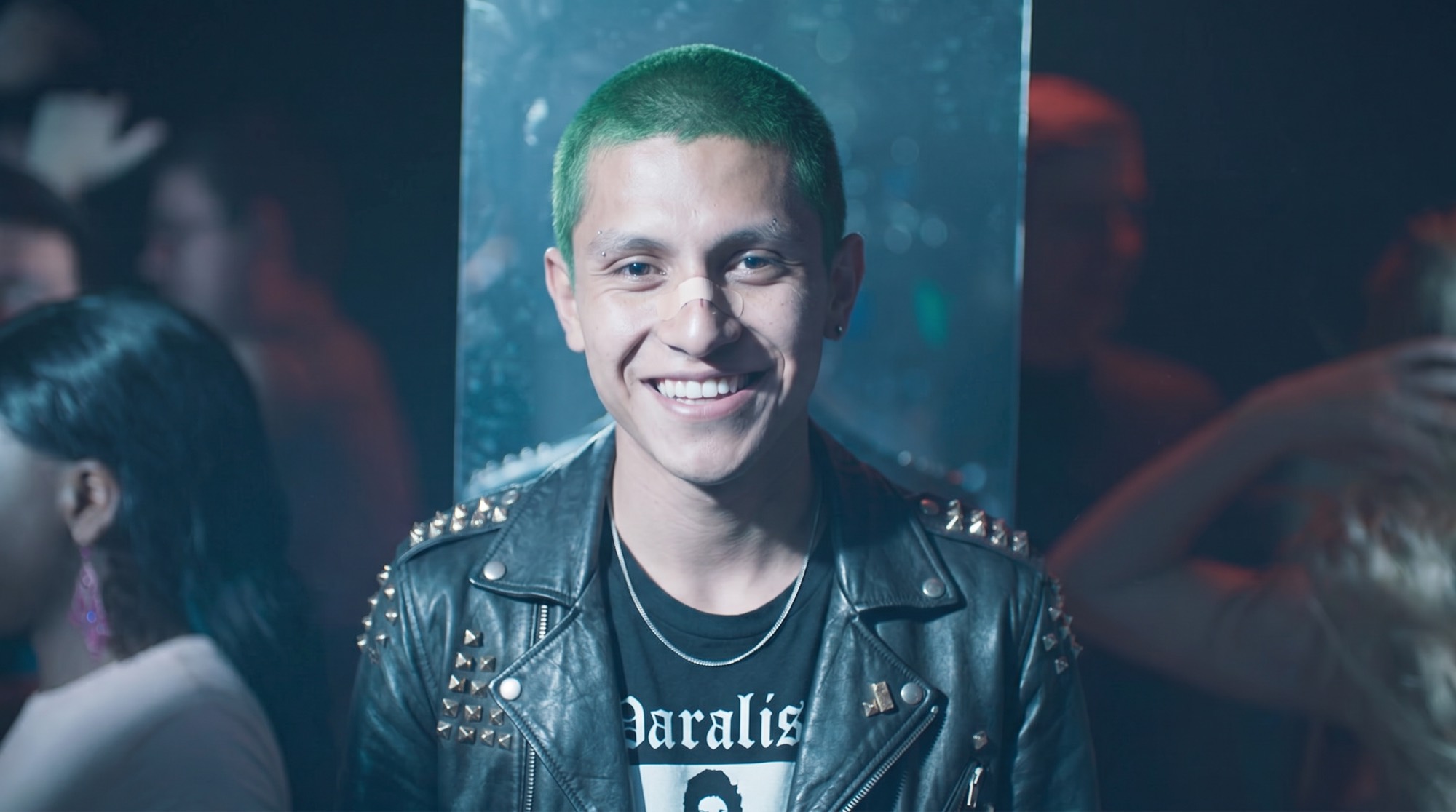 Nacho, pelo decolorado en verde y chamarra de piel con estoperoles.