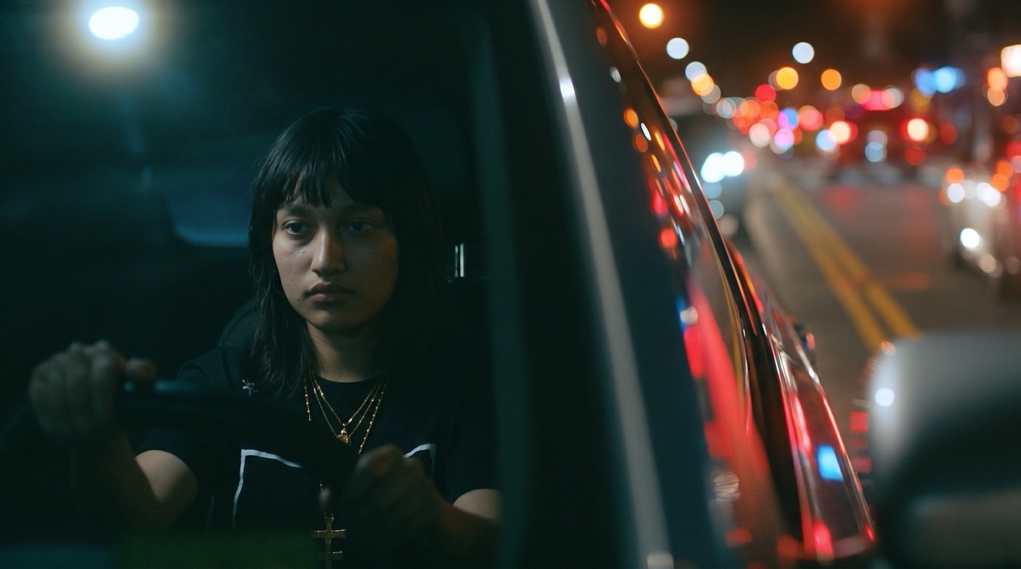 Elena al volante del Tsuru rojo, con el tráfico nocturno detrás.