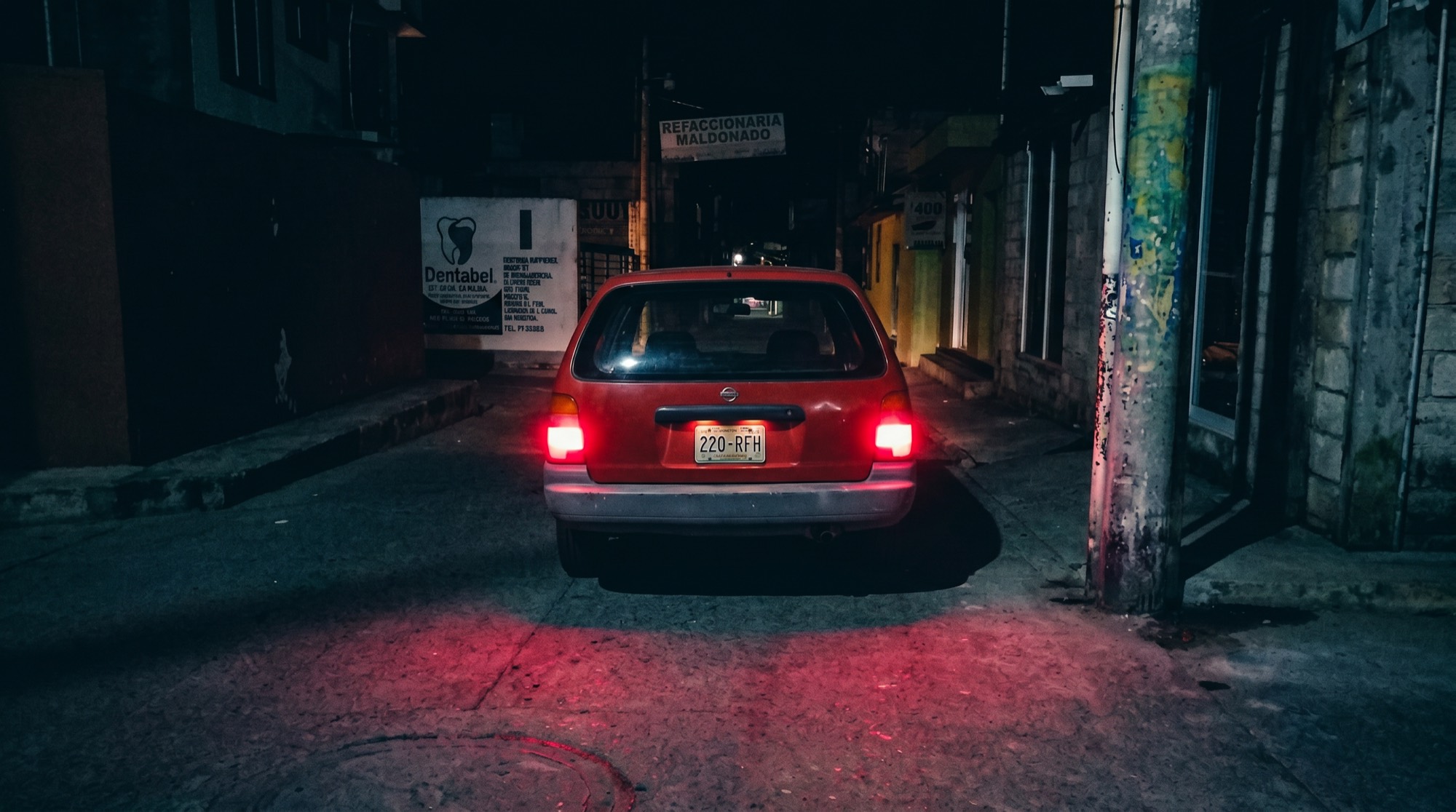 El Tsuru rojo detenido en una calle de noche, las luces de freno encendidas sobre el asfalto.